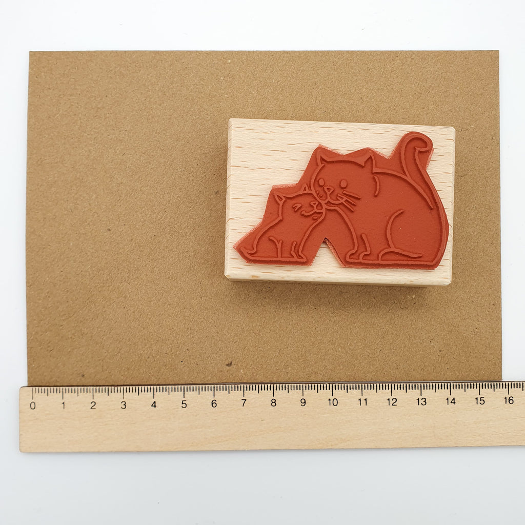 Stempel aus rotem Gummi mit dem Motiv einer kleinen und einer großen Katze auf einem braunen Briefumschlag mit Lineal