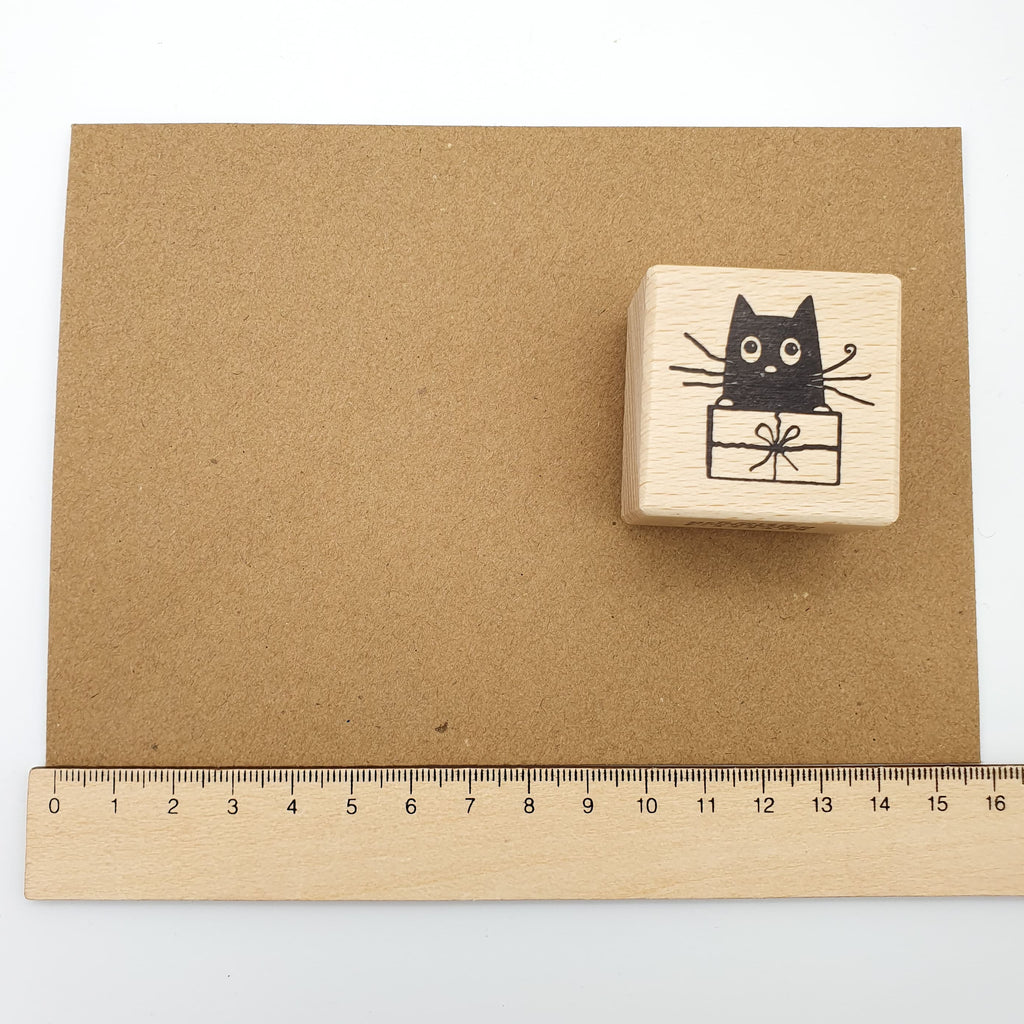 Stempel mit dem Motiv einer Katze, die in einem Geschenk sitzt auf einem braunen Briefumschlag mit Lineal