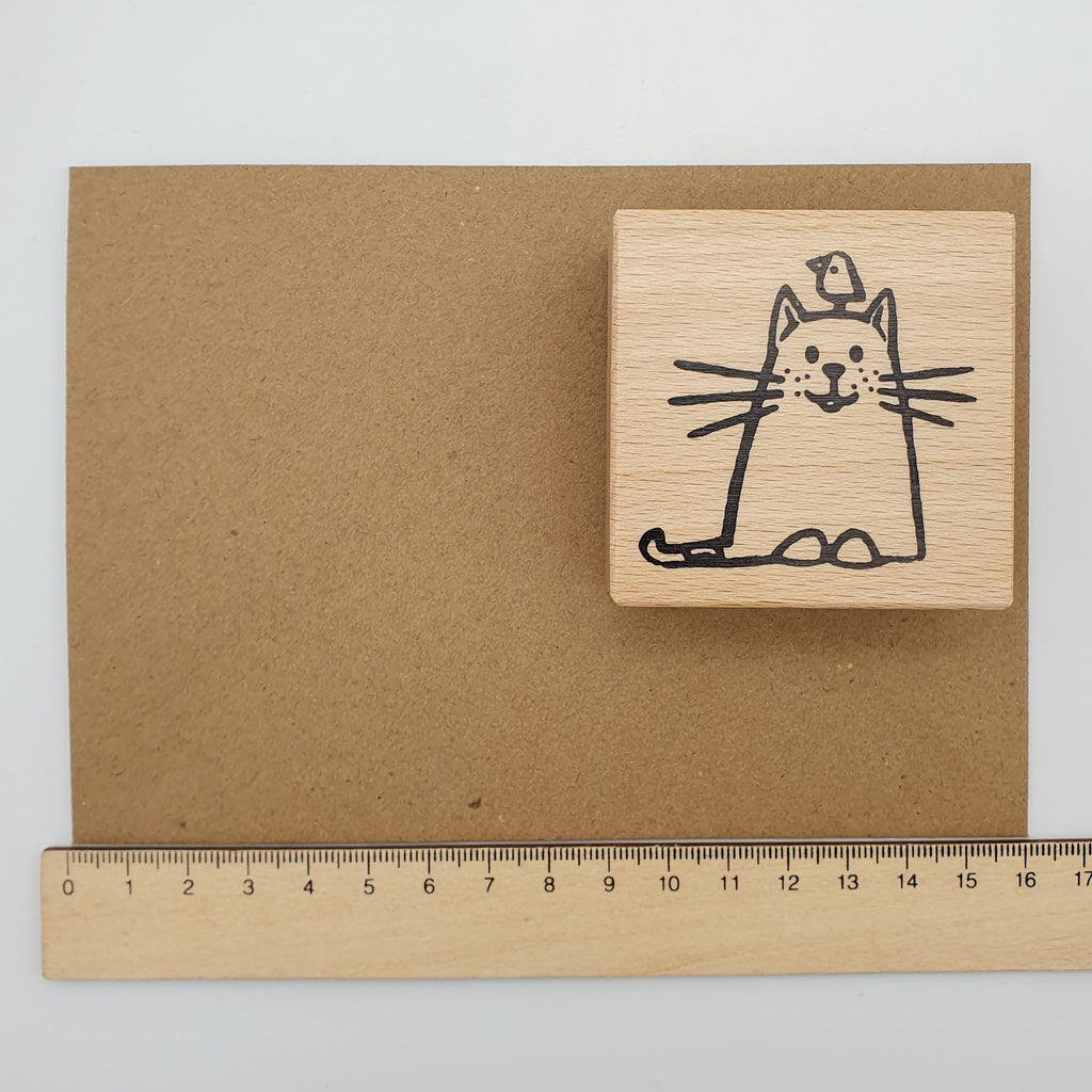 Stempel mit dem Motiv einer Katze und einem Vogel auf ihrem Kopf auf einem braunen Briefumschlag mit Lineal