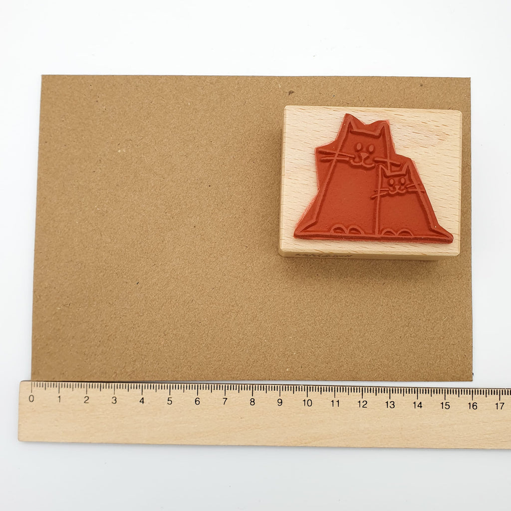 Stempel aus rotem Gummi mit dem Motiv einer kleinen und einen großen Katze auf einem braunen Briefumschlag mit Lineal