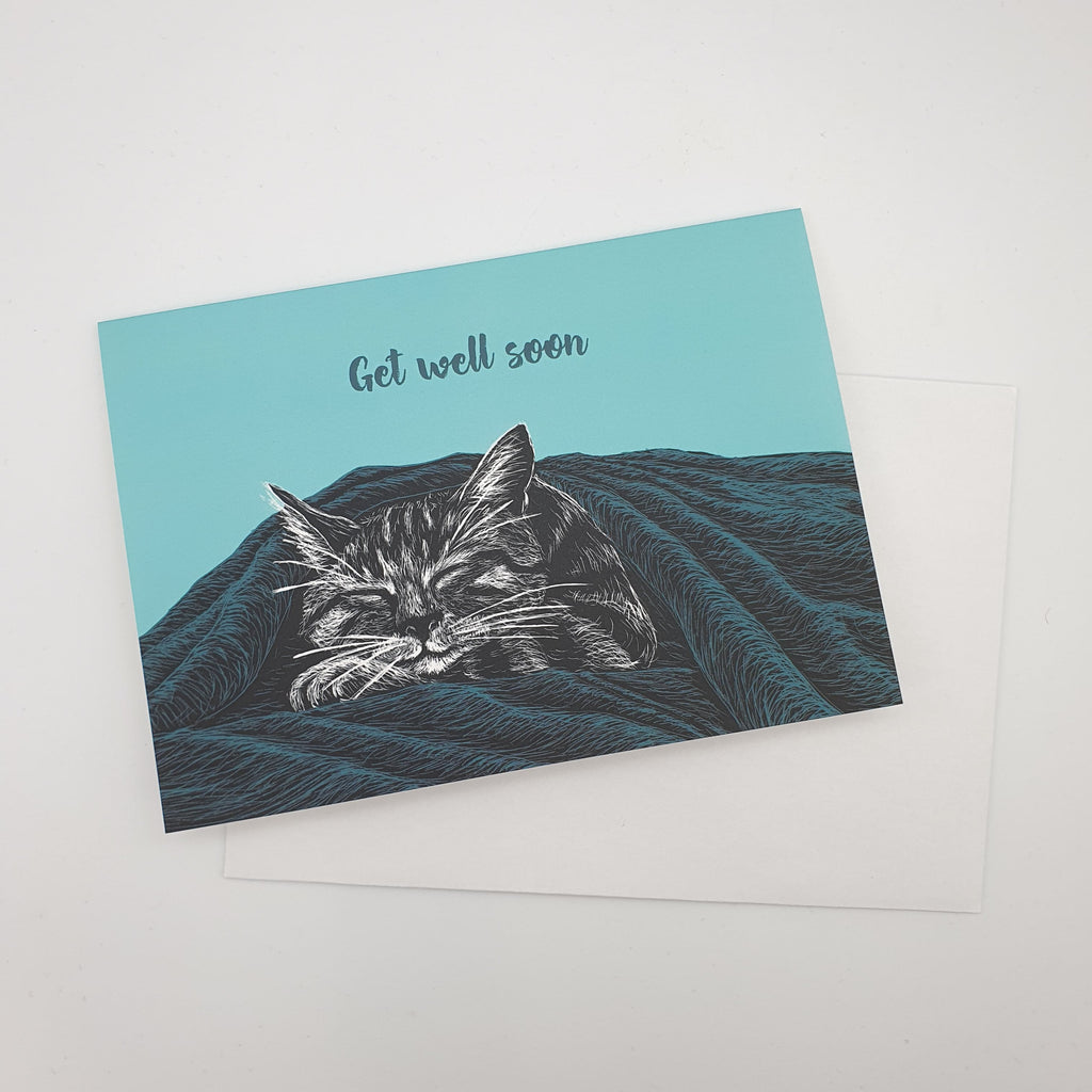Illustrierte Postkarte in türkis mit einer Katze, die zufrieden unter einer Decke schläft. Aufschrift: "Get well soon"