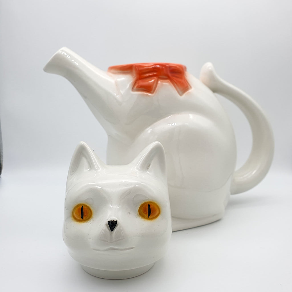 Weiße Kaffee- oder Teekanne in Form einer Katze mit einer roten Schleife