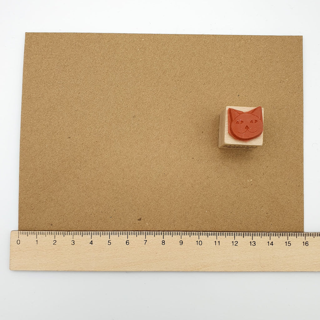 Stempel aus rotem Gummi in Form eines Katzenkopfes auf einem braunen Briefumschlag mit Lineal