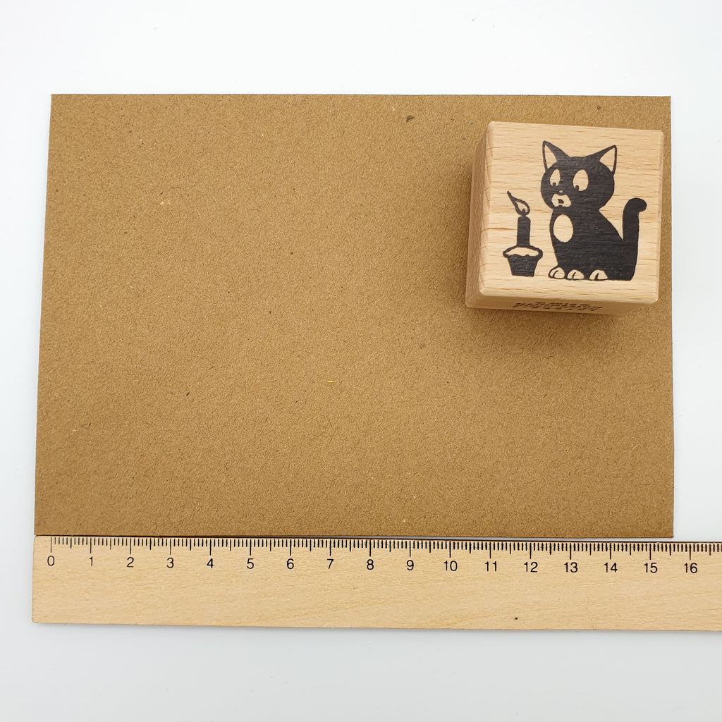 Stempel mit dem Motiv einer Katze, die eine Kerze ausbläst auf einem braunen Briefumschlag mit Lineal