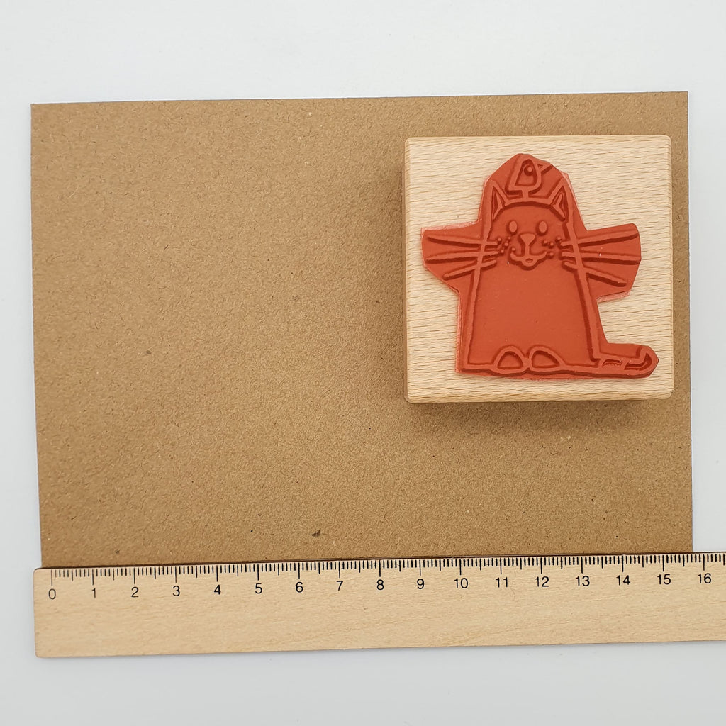 Stempel aus rotem Gummi mit dem Motiv einer Katze und einem Vogel auf ihrem Kopf auf einem braunen Briefumschlag mit Lineal