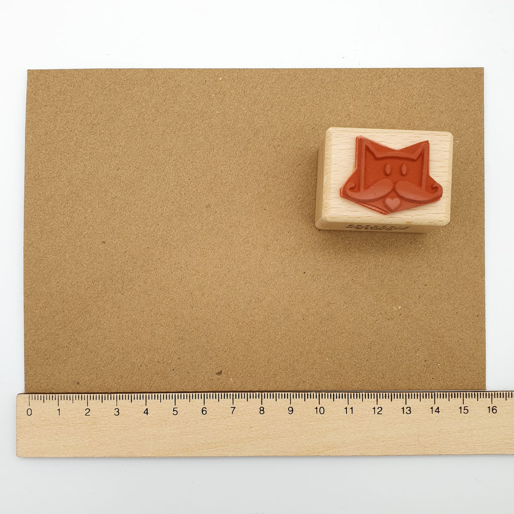 Stempel aus rotem Gummi mit dem Motiv einer Schnurrbart-Katze auf einem braunen Briefumschlag mit Lineal