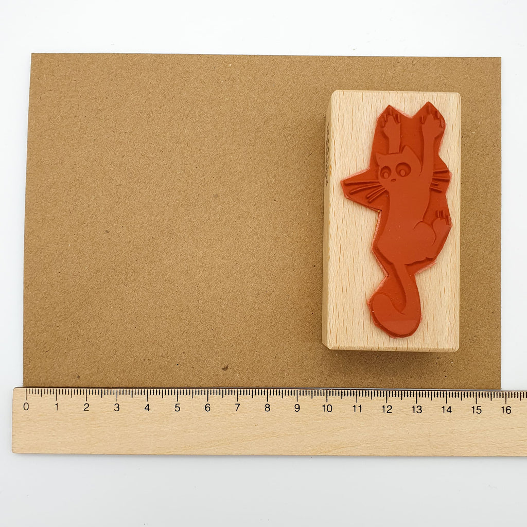 Stempel aus rotem Gummi mit dem Motiv einer krallenden Katze auf einem braunen Briefumschlag mit Lineal