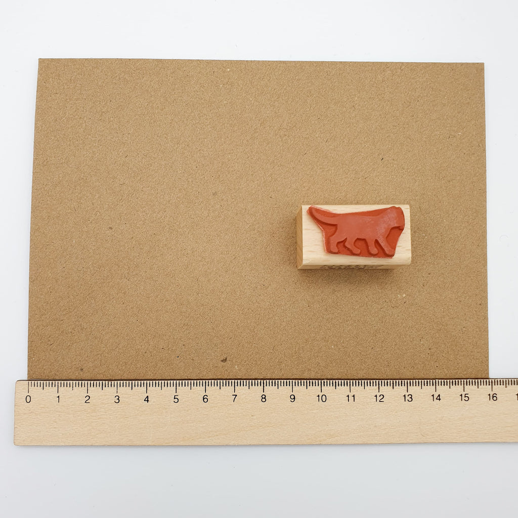 Stempel aus rotem Gummi mit dem Motiv einer laufenden schwarzen Katze auf einem braunen Briefumschlag mit Lineal