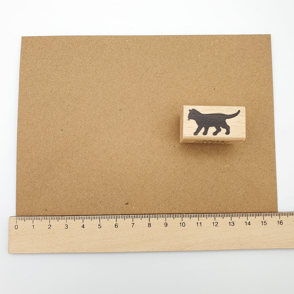 Stempel mit dem Motiv einer laufenden schwarzen Katze auf einem braunen Briefumschlag mit Lineal