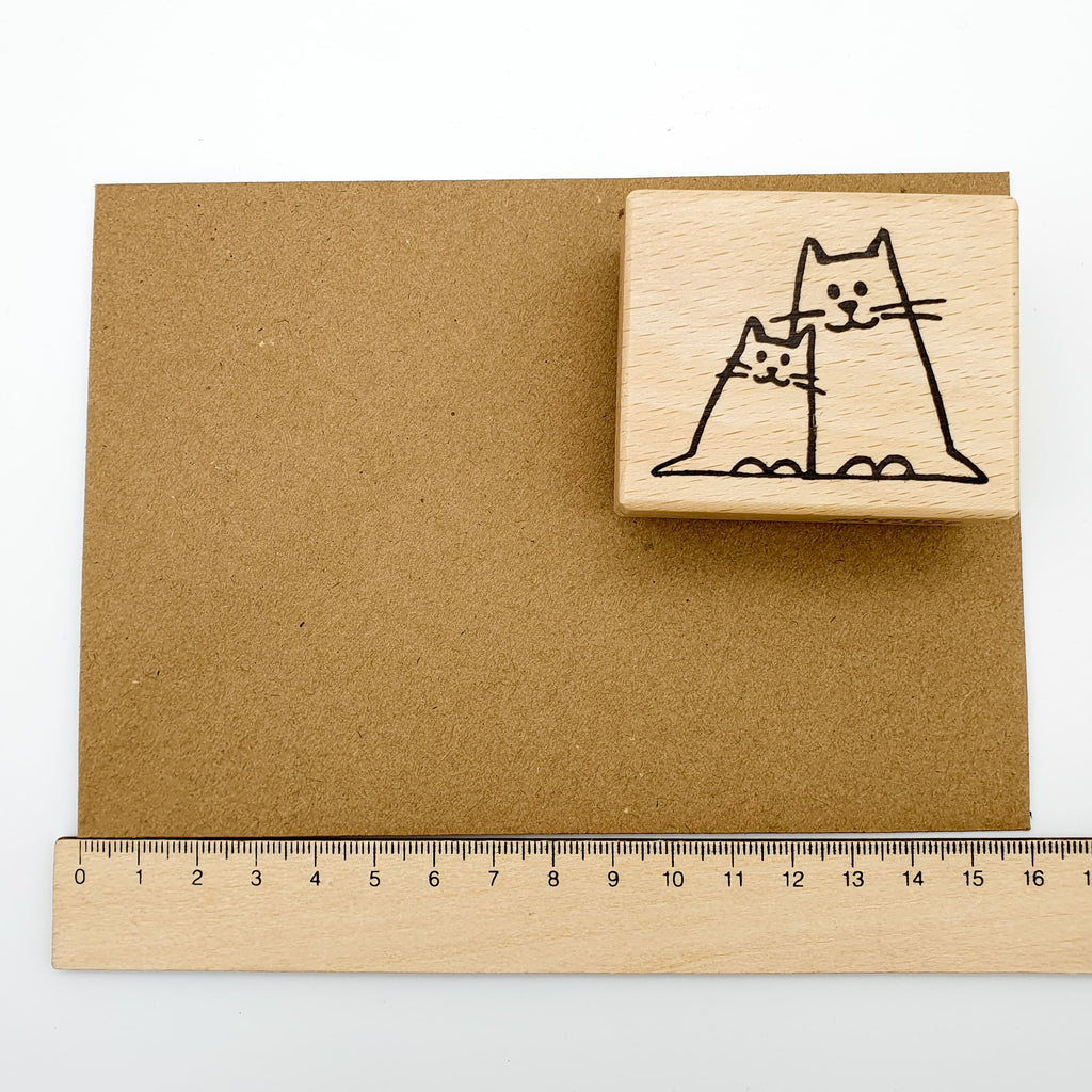 Stempel mit dem Motiv einer kleinen und einen großen Katze auf einem braunen Briefumschlag mit Lineal